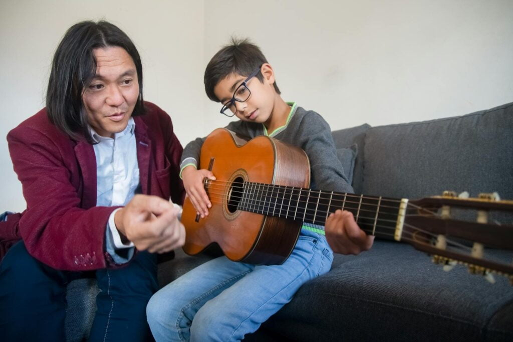 7historiasconsejosytestimoniosdemusicoterapeutas Un profesor de música enseñando a un niño a tocar la guitarra